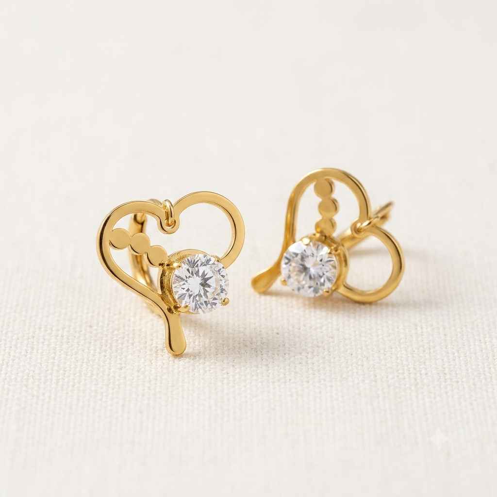 A pair of gold heart-shaped stud earrings with a clear round-cut gemstone, displayed on a textured off-white fabric background.