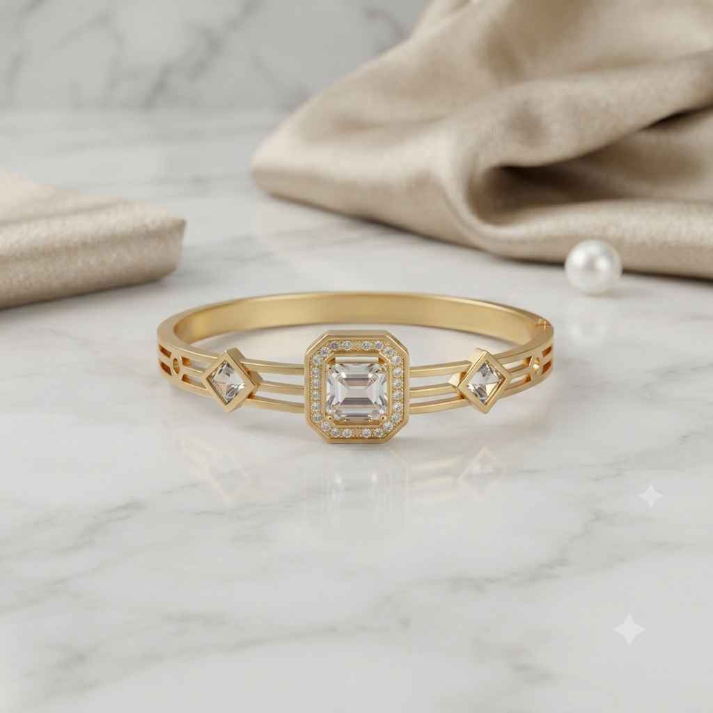 A gold bangle ring with a central square clear gemstone and diamond-cut side stones, displayed on a white marble surface with beige fabric and a pearl in the background.