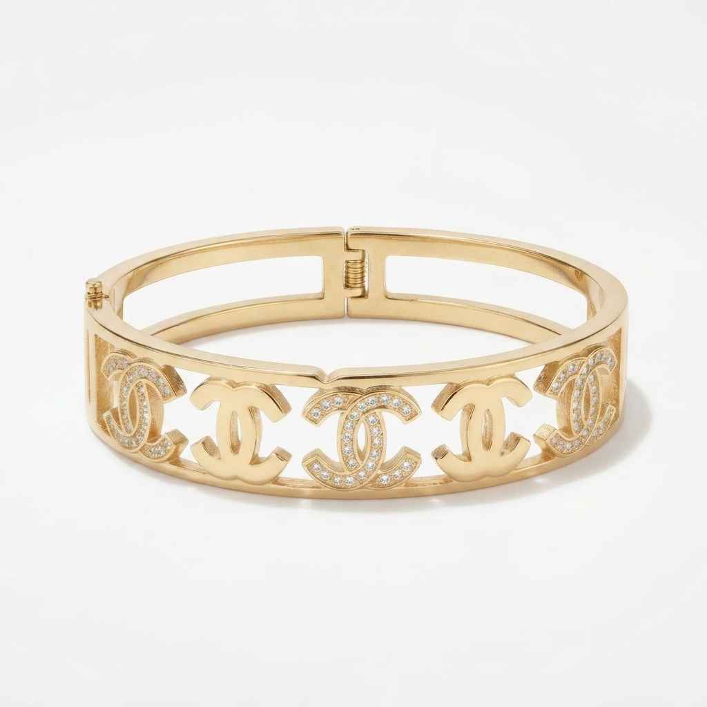 A gold-tone metal bangle bracelet featuring four interlocking Chanel CC logos, some embellished with small clear crystals, set against a plain white background.