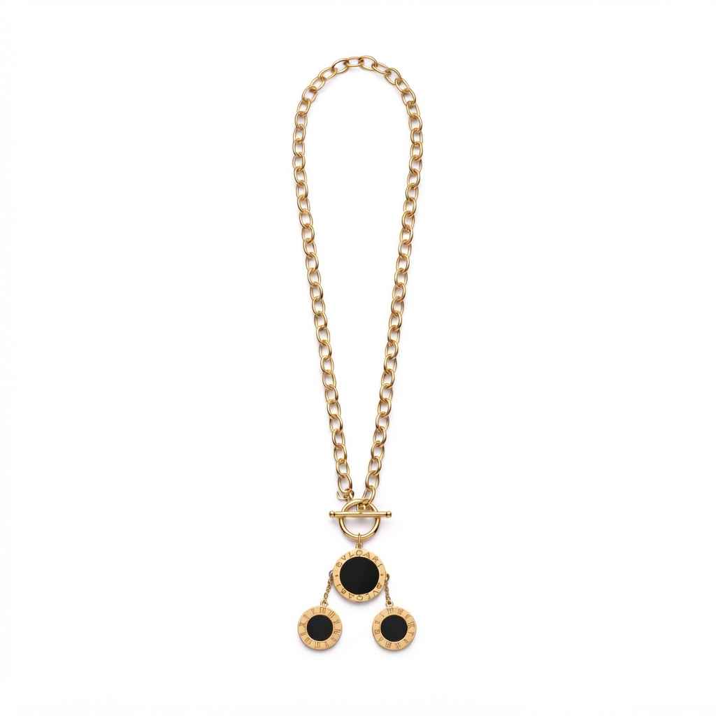 A gold chain necklace with a toggle clasp and a pendant featuring three circular black inlays set in a textured gold frame, displayed on a solid white background.