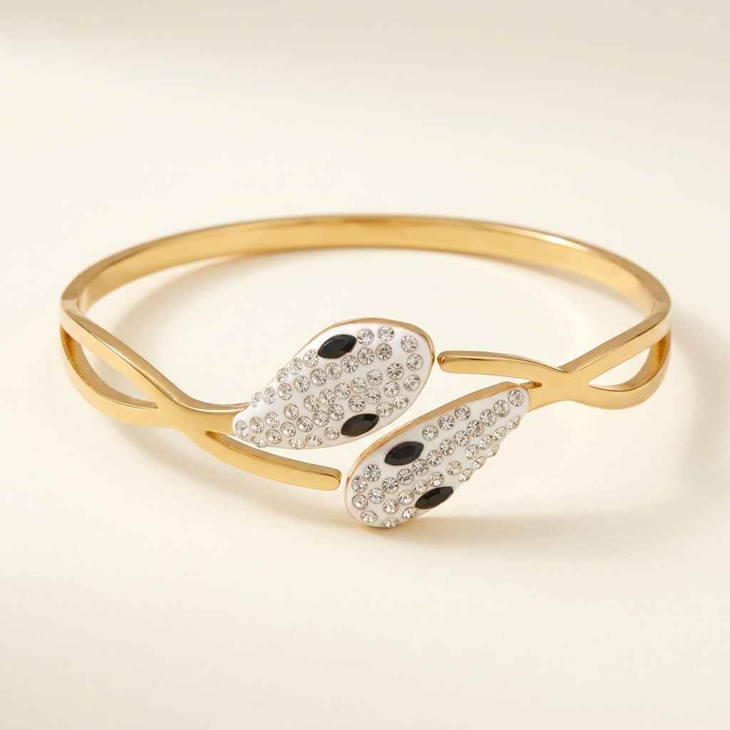 Gold-tone open cuff bangle bracelet featuring two stylized wing-like charms paved with clear rhinestones and accented with two black oval stones each, shown on a warm off-white background.