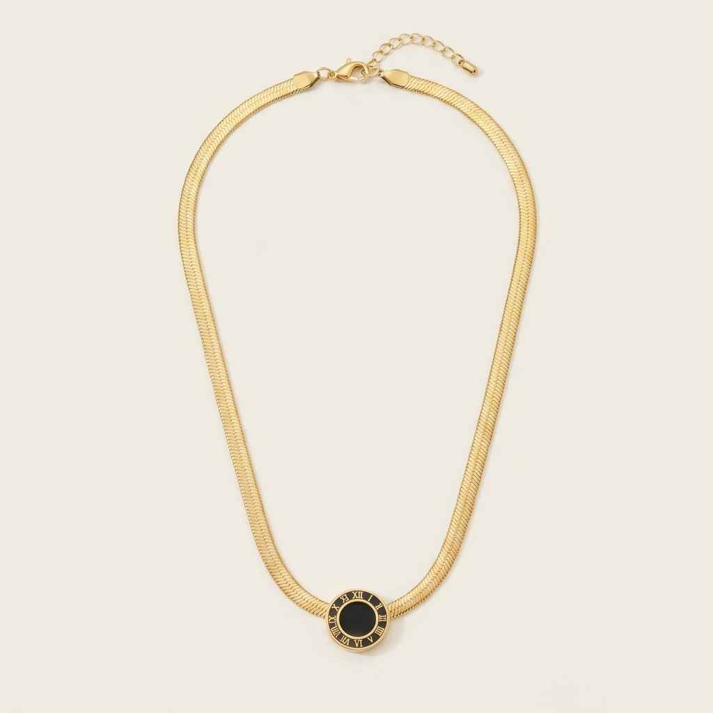 A gold snake chain necklace with a central oval pendant featuring a black center and gold border, displayed on a light cream background.