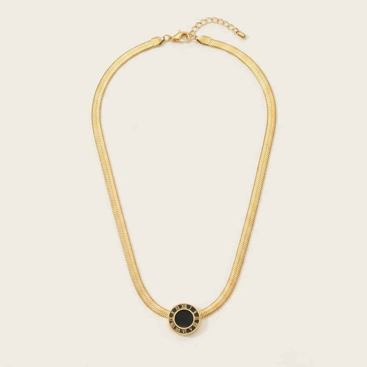 A gold snake chain necklace with a central oval pendant featuring a black center and gold border, displayed on a light cream background.